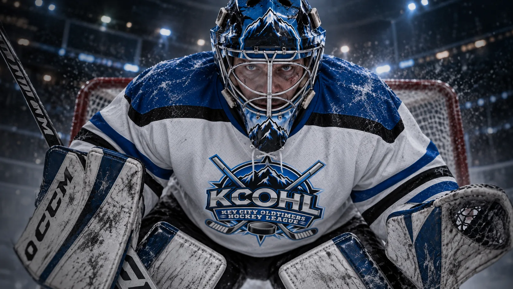 A KCOHL goalie in a white jersey crouched in the crease, eyes on the shooter